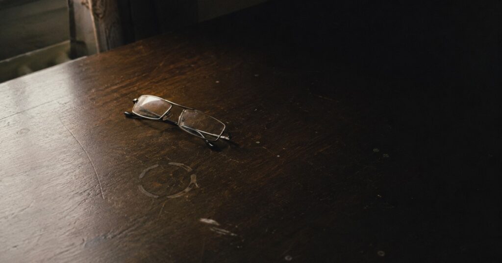 Gafas de leer dobladas sobre una mesa de madera oscura
